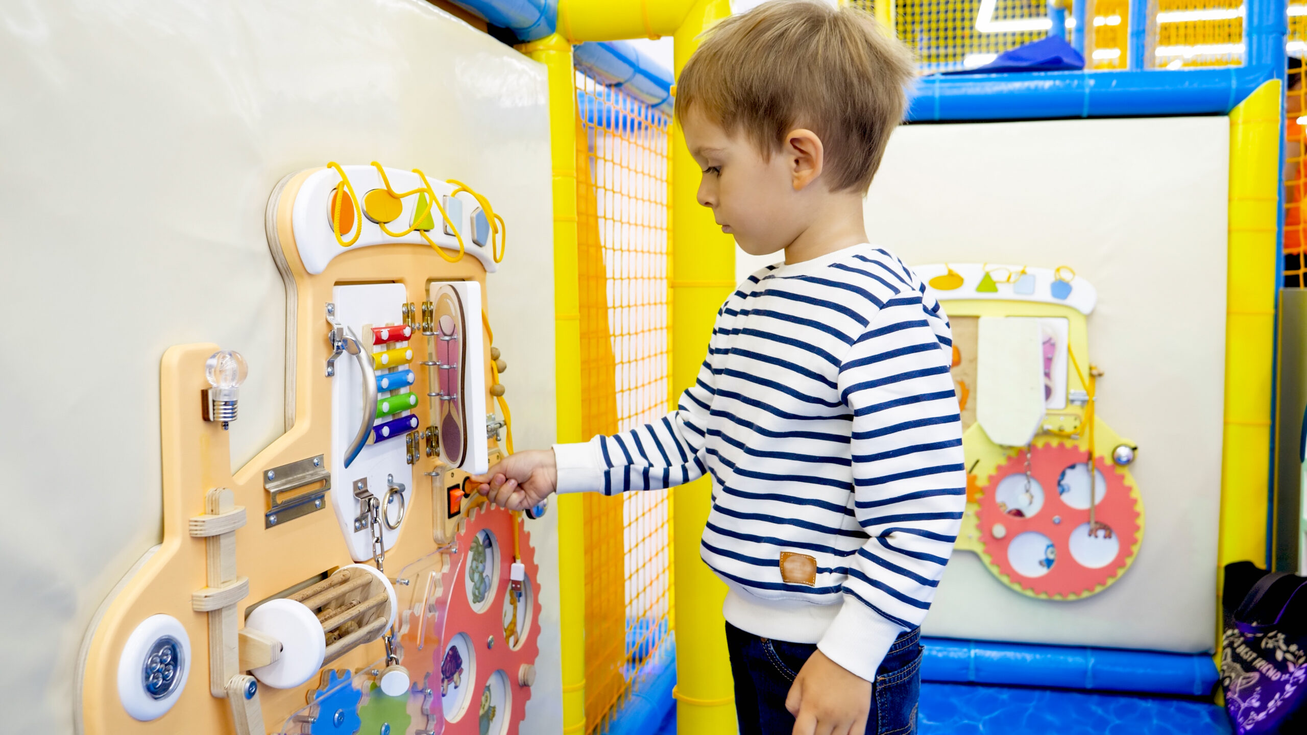 cute little boy playing with buttons and knobs on educational child's board in kindergarten